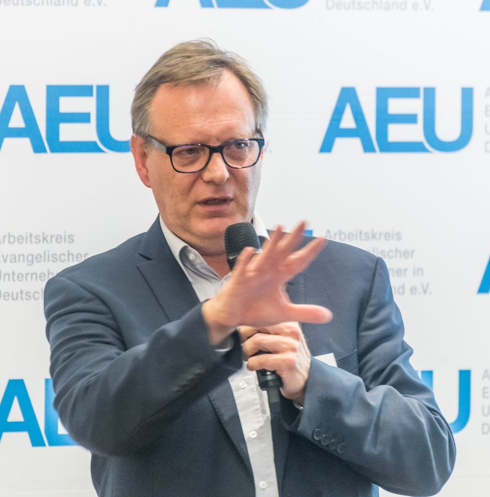 Jörg Kopecz spricht mit Mikrofon vor einer AEU-Wand