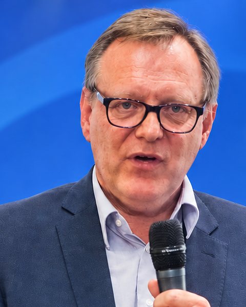 Prof. Dr. Jörg Kopecz spricht mit Mikrofon auf einer Bühne