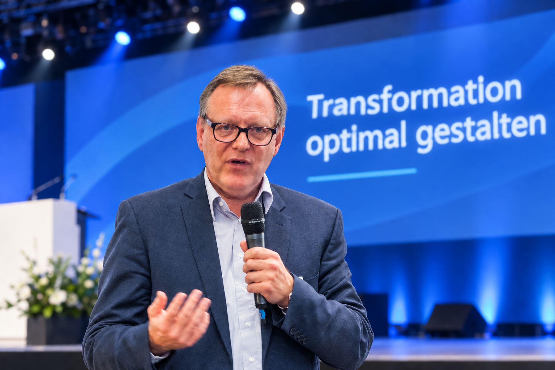 Jörg Kopecz spricht auf einer Bühne, im Hintergrund die Projektion „Transformation optimal gestalten“